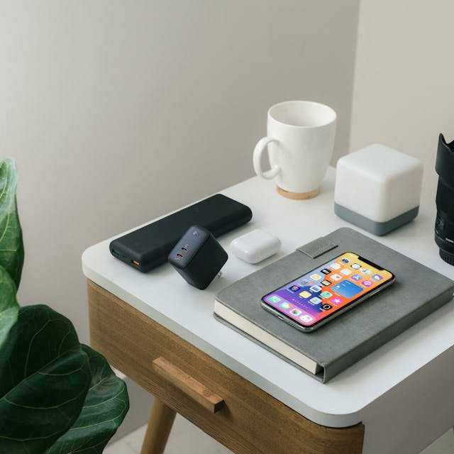 Smartphone on a wooden bedside table with a white mug and tech gadgets in a modern setup