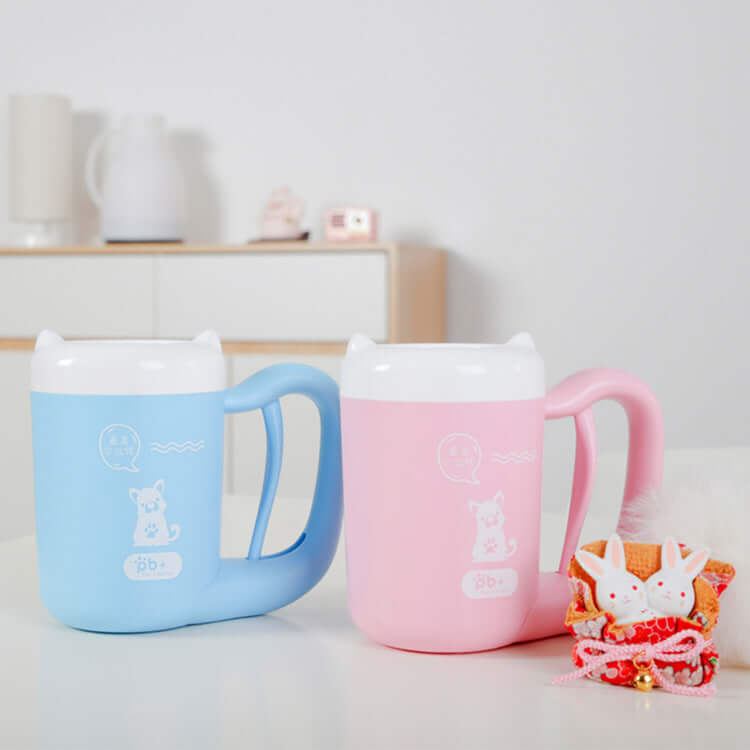 Two Pet Paw Cleaner Cup, one blue and one pink, with a small decorative item on a light surface.