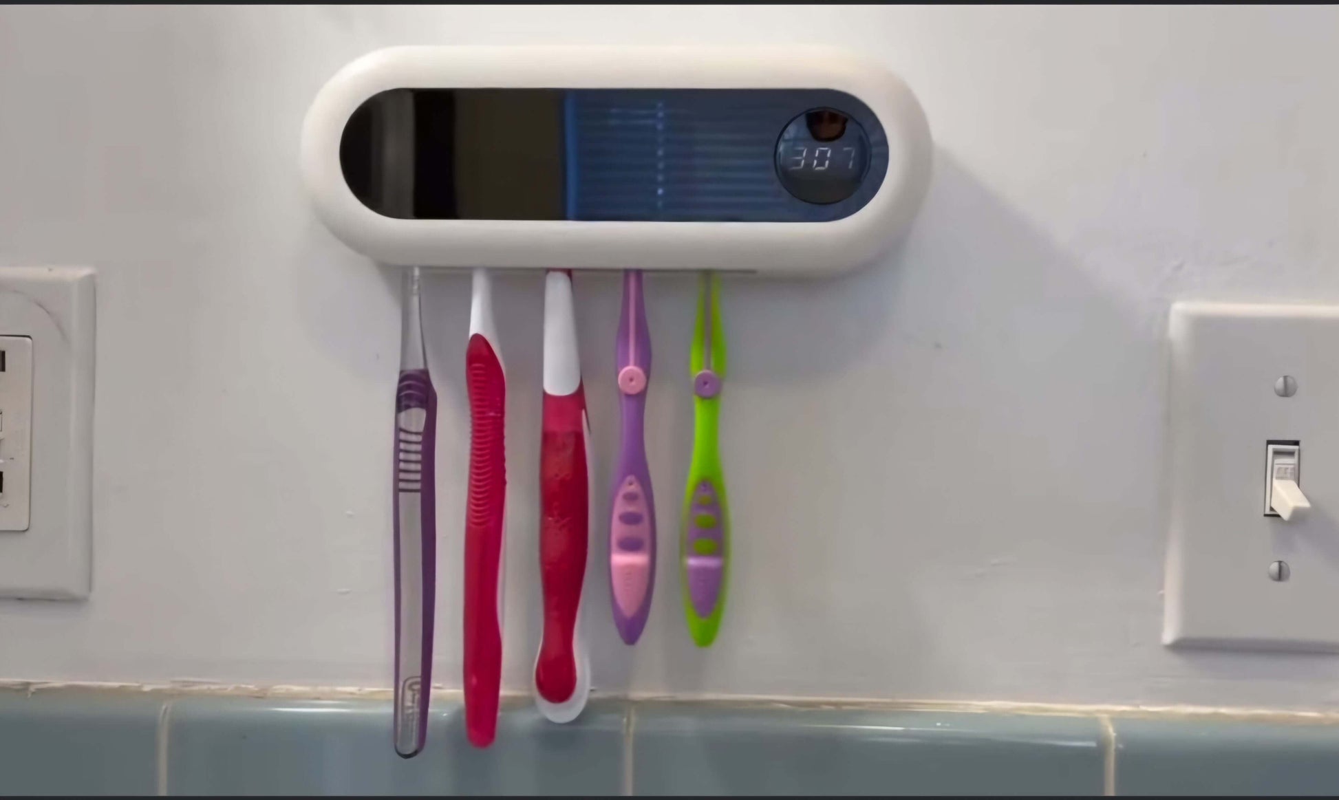 Colorful toothbrushes in a holder on a tiled bathroom wall.