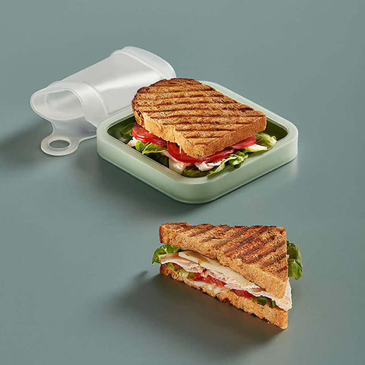 Sandwich in a green container with a lid, and a sliced sandwich on a gray background
